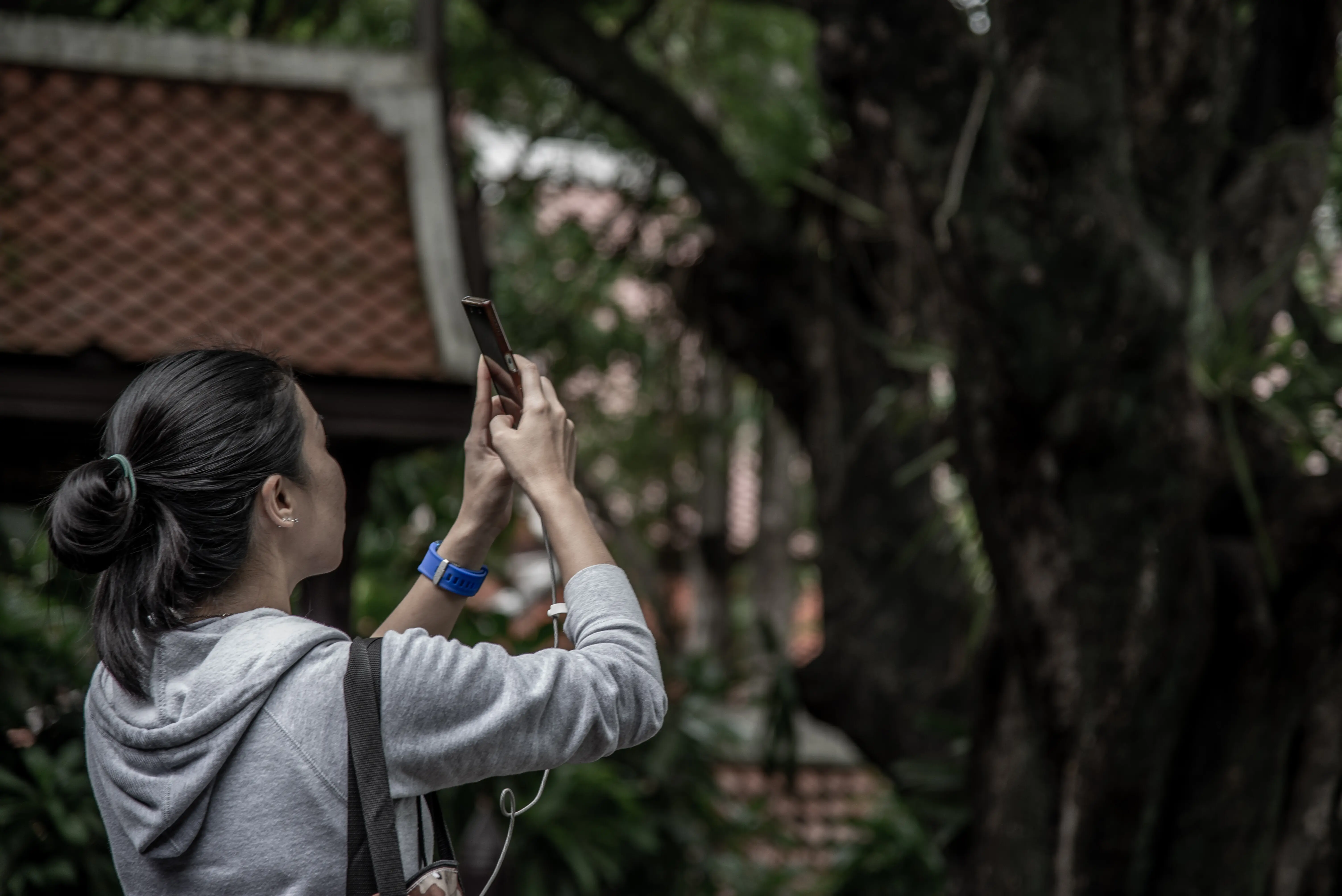 Eine Frau fotografiert mit einem Mobiltelefon, während sie an einem Baum steht.